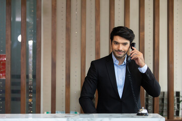 Handsome male receptionist is talking to a tourist who is making a online booking over the phone
