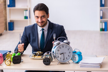 Young businessman employee eating alarm-clock