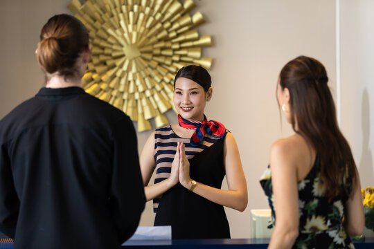 beautiful young asian woman receptionists working at a reception desk make pay respect (sawasdee) to customer.