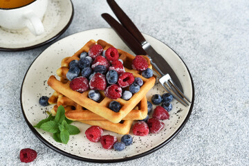 Vanilla Belgian waffles with berries and a cup of coffee for breakfast.