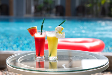 Two Colorful Tropical Cocktails on table neer swimming pool. Pineapple and watermelon smoothie.