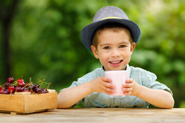 little boy holding glass of cherry yogurt outdoors