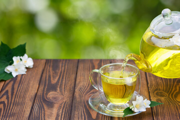green tea with jasmine flowers pouring from glass teapot in cup