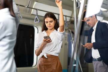 Young beautiful woman passenger using smartphone while going to working by public sky electric train - obrazy, fototapety, plakaty