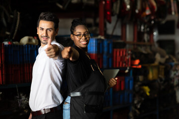 African American female employee worker and hispanic man manager working together at old auto and car parts warehouse store.