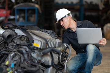 Mechanical man owner small business inspecting old car parts stock on laptop computer while working in old automobile parts large warehouse