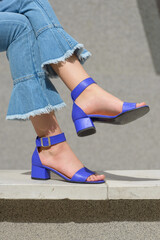 Women's legs in blue denim jeans and sandals in the city street. Trendy elegant casual outfit....