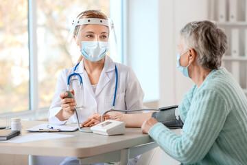 Obraz premium Doctor measuring blood pressure of senior woman in clinic