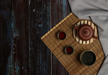 Chinese Tea Ceremony. Brown ceramic teapot and turquoise teacup. Green tea on a bamboo mat on an aged wooden table. Top view. Copy space