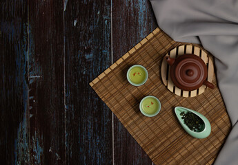 Chinese Tea Ceremony. Brown ceramic teapot and turquoise teacup. Green tea on a bamboo mat on an aged wooden table. Top view. Copy space