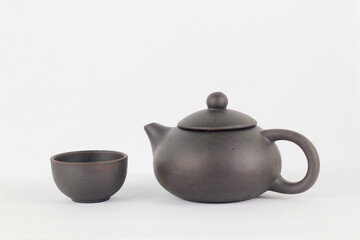 A Chinese black ceramic teapot and teacup isolated on a white background.