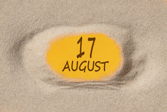 August 17. 17th day of the month, calendar date. Hole in sand. Yellow background is visible through hole. Summer month, day of the year concept