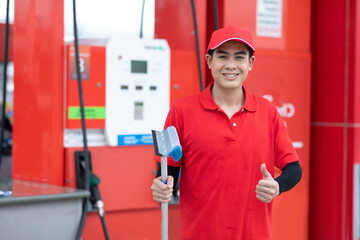 Portrait of Man worker in red uniform holding sponge clean windscreen of car while representing high quality service of gas fuel station