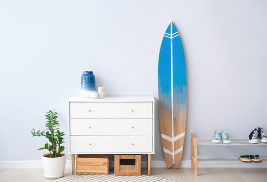 Interior of modern stylish hall with surfboard, shoe stand and chest of drawers