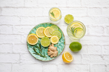 Glasses of healthy lemonade and plate with citrus fruits on brick background