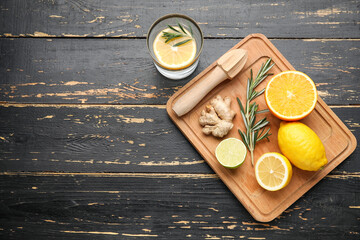 Glass of healthy lemonade, citrus fruits and squeezer on dark wooden background