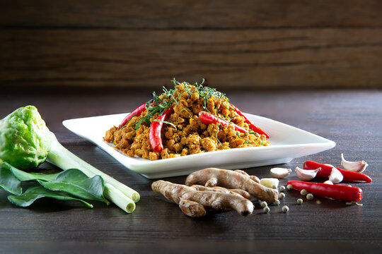 Spicy stir fry minced pork with curry paste (Thai call *Kua kling*) on dark brown wooden table