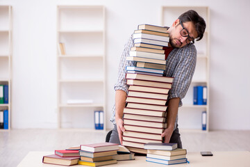 Young male student and too many books in the classroom