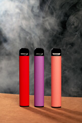 Colorful disposable electronic cigarettes on a black background with smoke. The concept of smoking,...