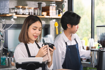 Two asian coffee waitress making cup of hot coffee latte in coffee shop cafe. Barista working with coffee machine in shop.