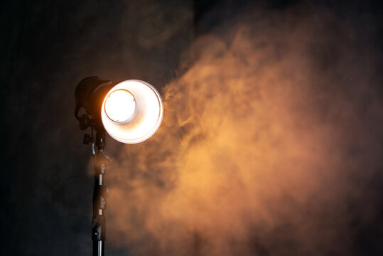 Beautiful studio light for a movie and TV show and photo on a dark background with smoke. A ray of light penetrates the smoke and darkness. 