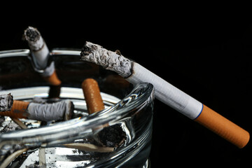 Ash tray with burning cigarettes on dark background, closeup