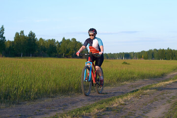 Obraz premium The girl rides a mountain bike on a field road. Endurance training, tempo or interval. Healthy lifestyle. Weight loss by sports. Hobby of a modern person.
