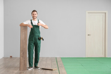 Carpenter showing thumb-up during installing of laminate flooring in room