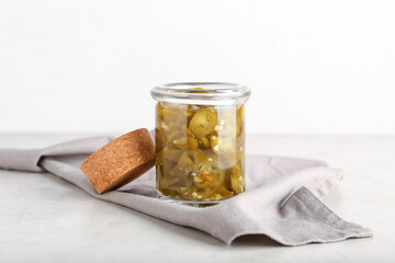 Glass jar with canned jalapeno on light background