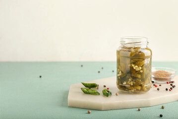 Glass jar with canned jalapeno on color background
