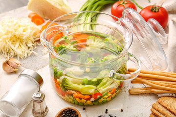 Stylish cooking pot with tasty soup and ingredients on light background