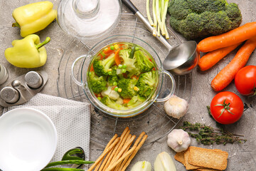 Stylish cooking pot with tasty soup and ingredients on grunge background