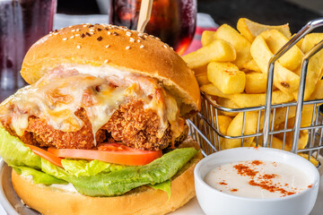 A chicken parma burger with lettuce and tomato on a white plate with french fries in a wire basket...