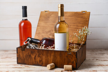 Box with bottles of wine and corkscrew on light wooden background
