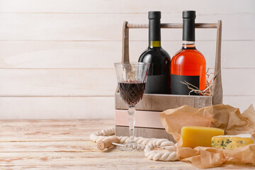 Naklejka premium Box with bottles of wine, cheese and glass on light wooden background