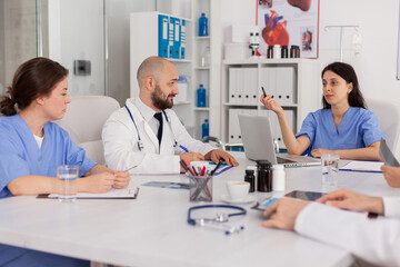 Fototapeta premium Medical nurse discussing disease examination with research team sitting in clinical meeting room. Professional physicians doctors prescribing pills medication treatment against sickness