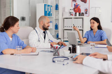 Medical nurse discussing disease examination with research team sitting in clinical meeting room. Professional physicians doctors prescribing pills medication treatment against sickness