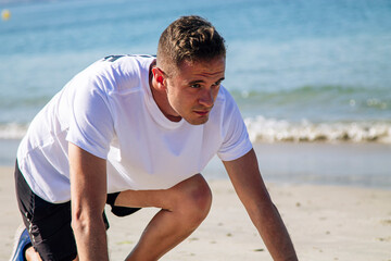 young man in starting position for jogging on the beach