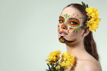 Young woman with painted skull on her face for Mexico's Day of the Dead against light background
