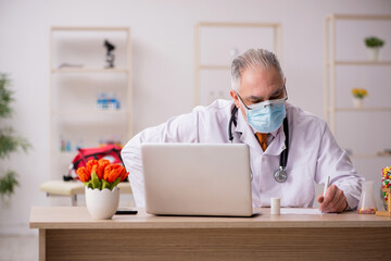 Old male doctor working in the clinic during pandemic