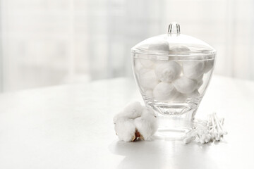 Container with soft cotton wool and swabs on table in room