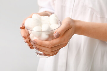 Woman with bowl of soft cotton wool on light background, closeup