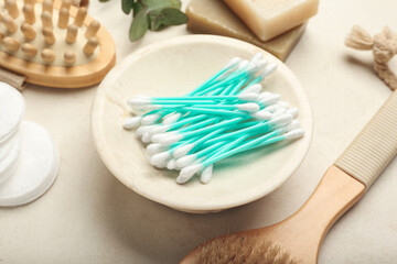 Fototapeta na wymiar Plate with cotton swabs, comb, brush and buds on light background, closeup