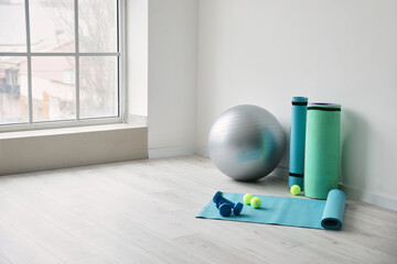 Set of sports equipment with fitness ball near light wall