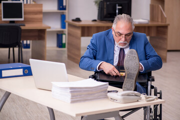 Old businessman employee in wheel-chair working in the office