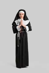 Young praying nun on light background