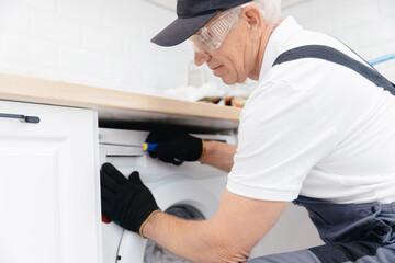 Naklejka na ściany i meble Service for repair, plumber man in uniform repairing washing machine