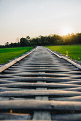 Obraz premium Selective focus on wooden bamboo path bridge spanning in the green rice field countryside with sun light in the evening for Thailand tourism travel concept