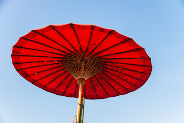 Under red handmade paper umbrella in Thai northern style with clear blue sky © gjeerawut