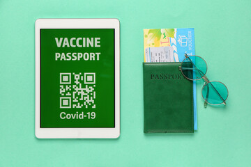 Electronic immune passport on screen of tablet computer, ticket and travel voucher on color background